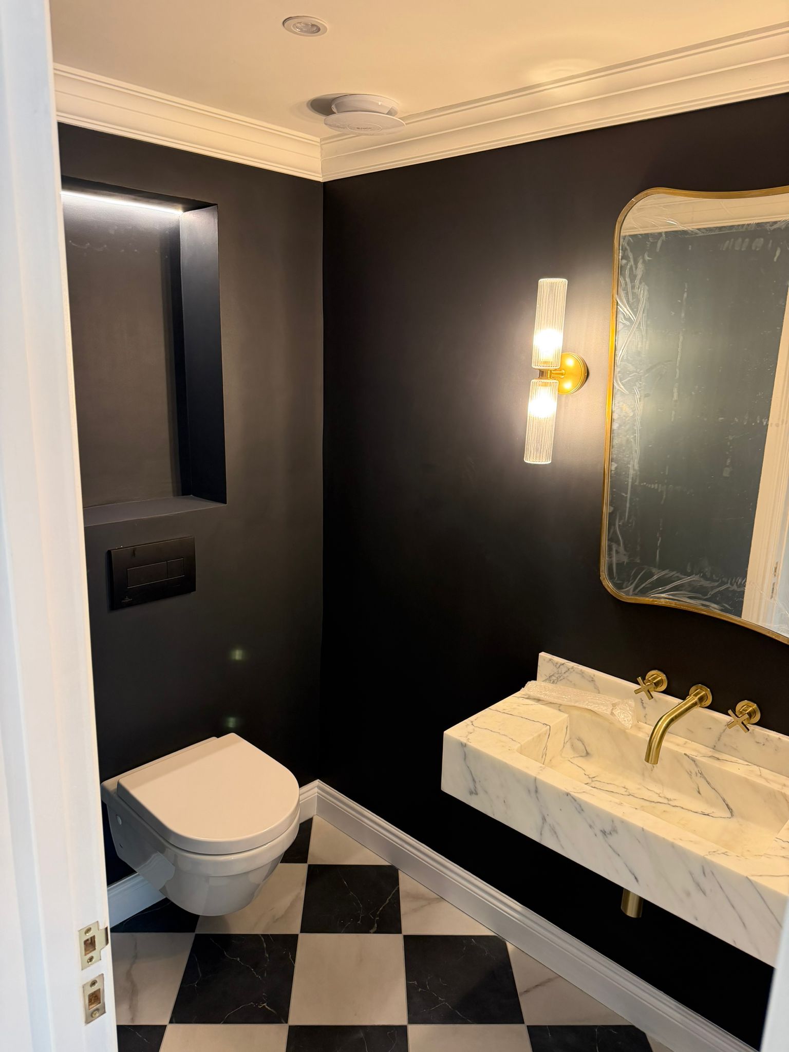 Dark cloakroom with veined marble basin and illuminated mirror