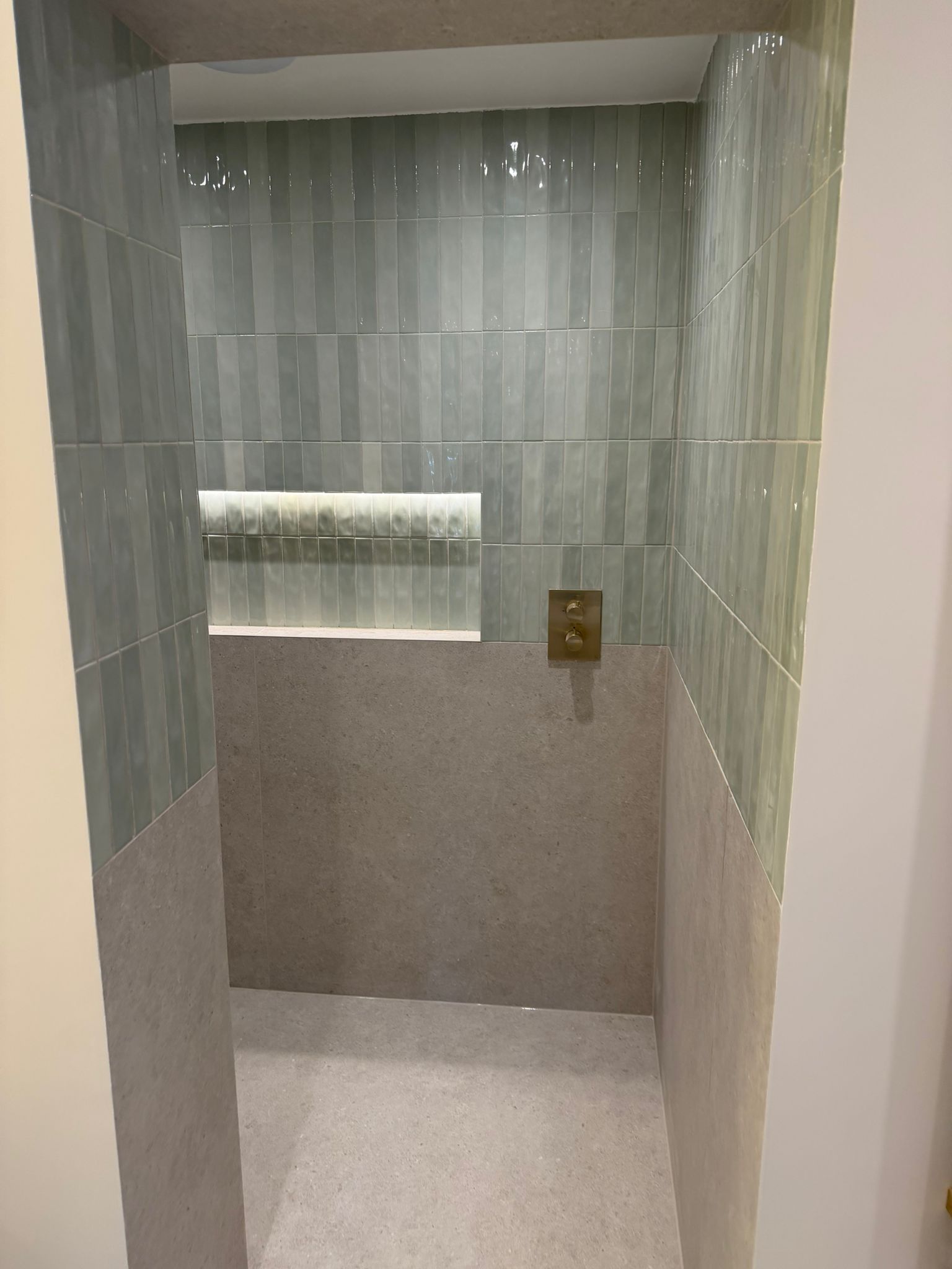 Walk-in shower lined with pale green vertical tiles and an illuminated niche