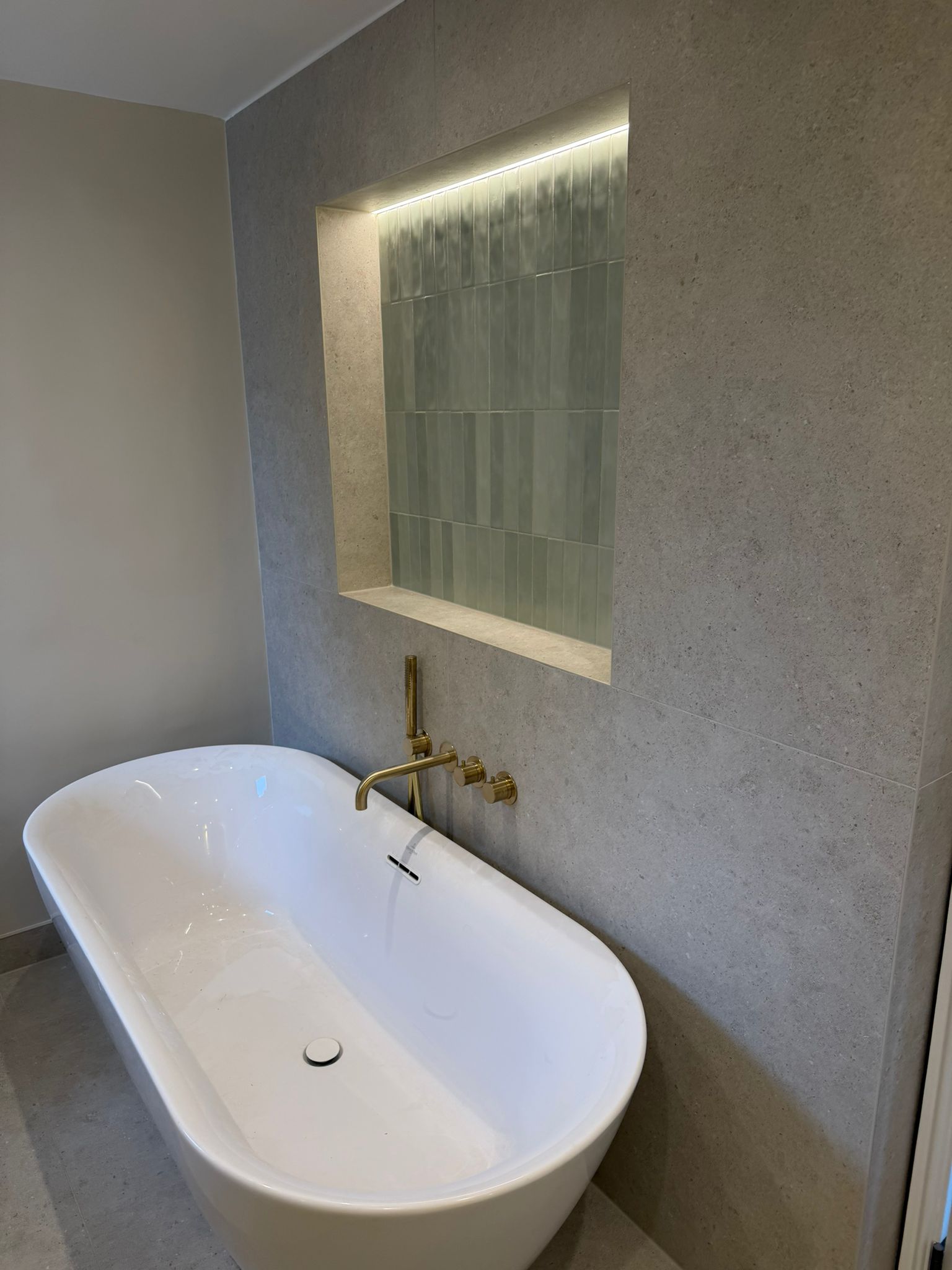 Freestanding bath below a recessed shelf in a pale tiled bathroom