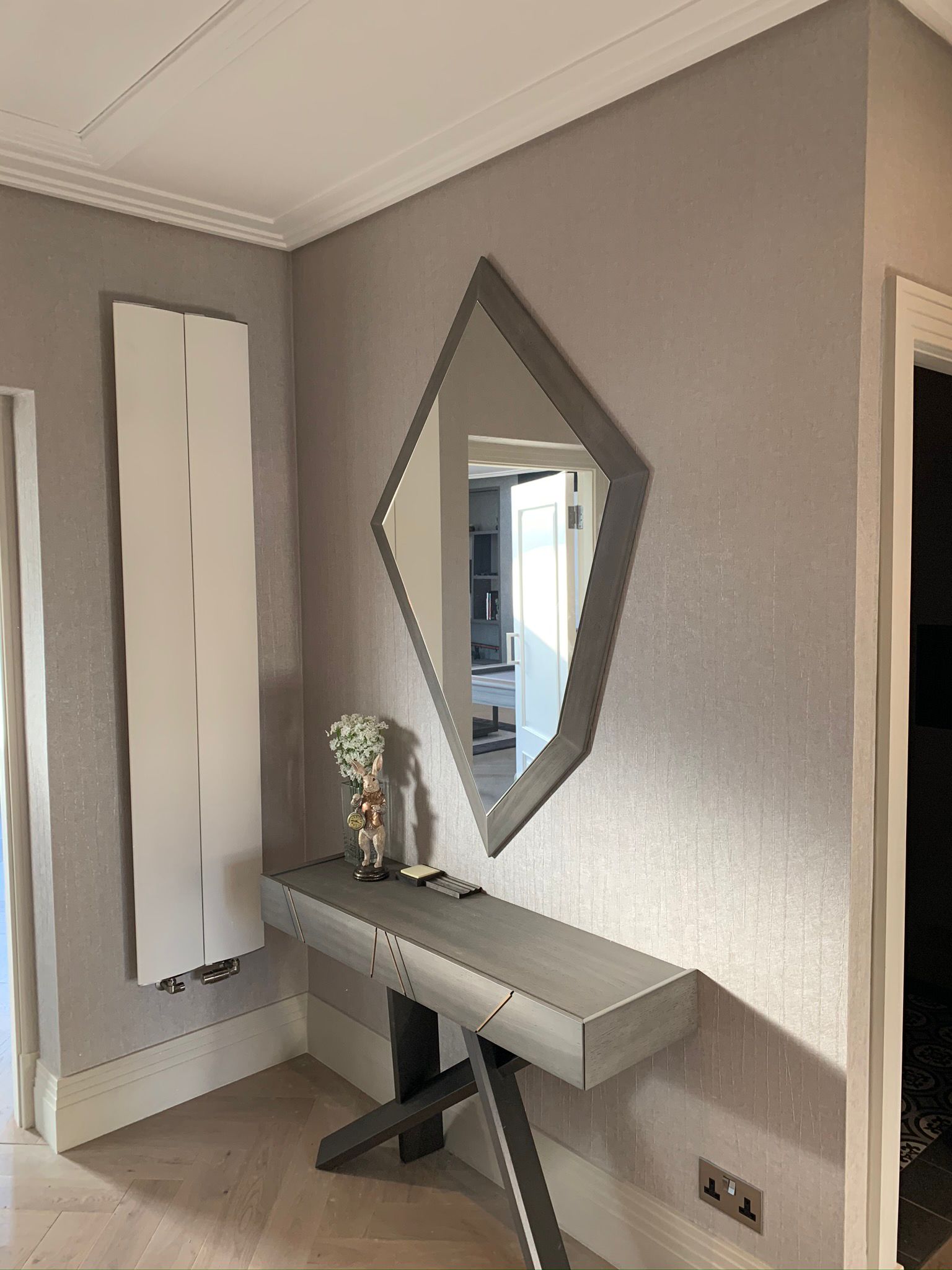 Hall console table and geometric mirror against a textured wall