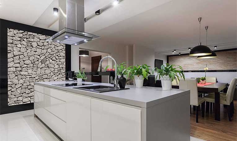 White kitchen island beneath pendant lights beside a stone feature wall